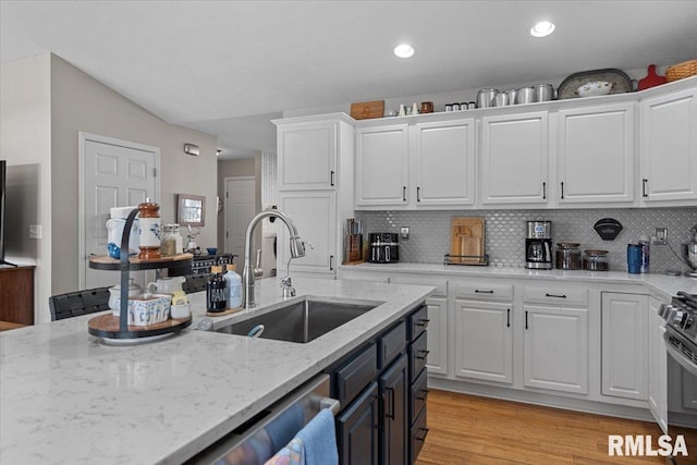 kitchen featuring light wood-type flooring, light stone counters, decorative backsplash, white cabinets, and a sink