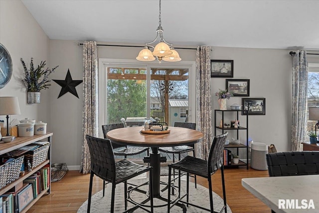 dining space with a wealth of natural light, light wood finished floors, baseboards, and an inviting chandelier