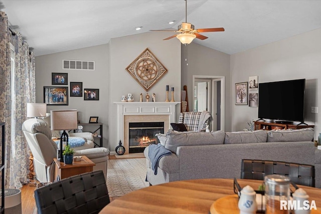 living room featuring visible vents, light wood-style flooring, a ceiling fan, a fireplace, and lofted ceiling