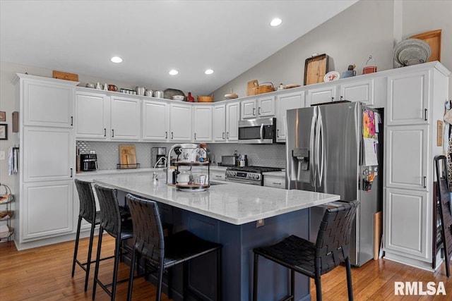 kitchen featuring a breakfast bar area, white cabinetry, stainless steel appliances, and vaulted ceiling