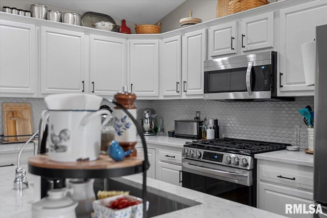 kitchen with decorative backsplash, white cabinets, light stone countertops, and appliances with stainless steel finishes