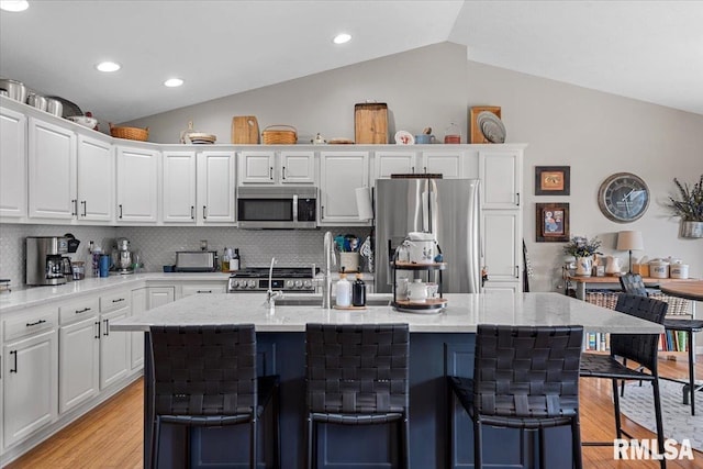 kitchen with lofted ceiling, white cabinets, light wood-style floors, and stainless steel appliances