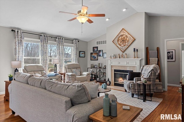 living area with visible vents, ceiling fan, lofted ceiling, a fireplace, and wood finished floors