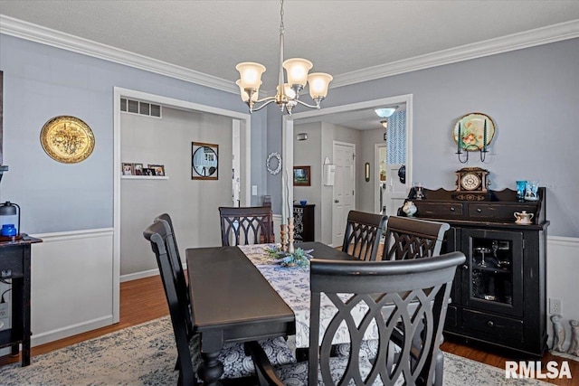 dining room with visible vents, wood finished floors, crown molding, baseboards, and a chandelier