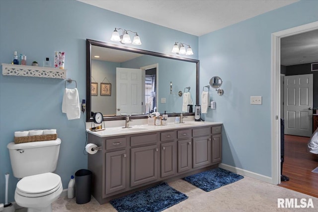 full bath featuring double vanity, toilet, baseboards, and a sink