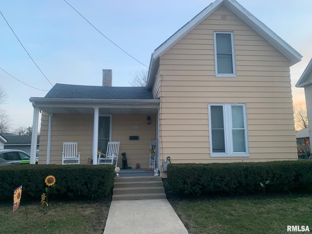 view of front facade featuring roof with shingles, a porch, and a chimney