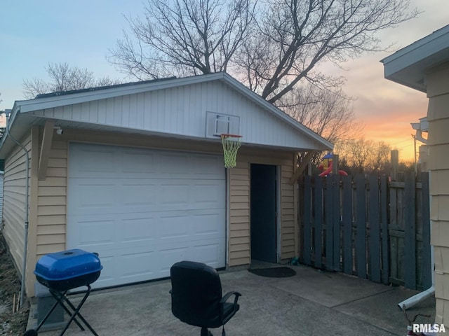 garage at dusk featuring a detached garage and fence