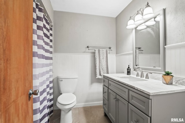 full bath featuring vanity, a shower with shower curtain, a wainscoted wall, tile patterned floors, and toilet