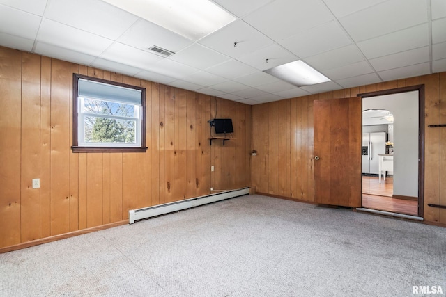 carpeted empty room featuring a baseboard heating unit, baseboards, visible vents, and a drop ceiling