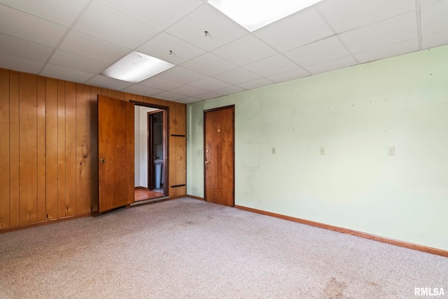 carpeted spare room featuring baseboards, a paneled ceiling, and wooden walls