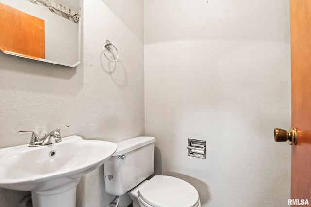 half bath featuring toilet, a textured wall, and a sink