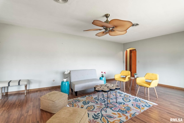 living area with a ceiling fan, wood finished floors, baseboards, and arched walkways