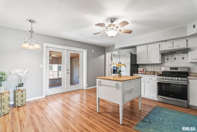 kitchen with under cabinet range hood, light wood-type flooring, decorative backsplash, appliances with stainless steel finishes, and french doors