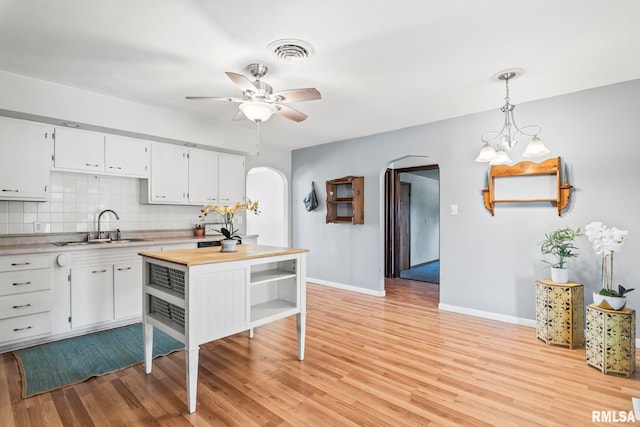 kitchen with visible vents, light wood-type flooring, decorative backsplash, arched walkways, and a sink