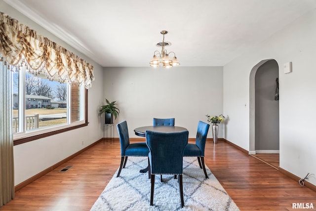 dining area featuring visible vents, baseboards, wood finished floors, arched walkways, and a notable chandelier