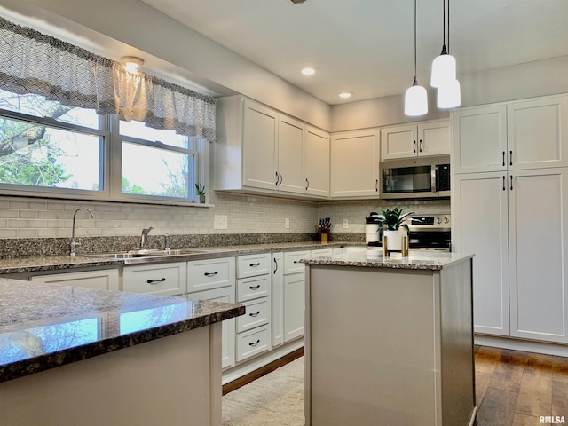 kitchen with a sink, backsplash, wood finished floors, stainless steel appliances, and white cabinets