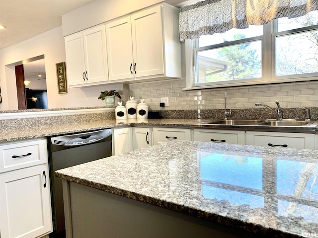 kitchen featuring light stone countertops, white cabinetry, a sink, dishwasher, and backsplash