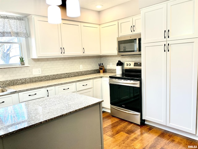 kitchen with tasteful backsplash, appliances with stainless steel finishes, wood finished floors, and white cabinets