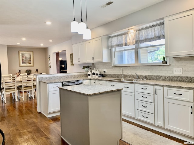 kitchen featuring a sink, backsplash, black dishwasher, dark wood finished floors, and a peninsula