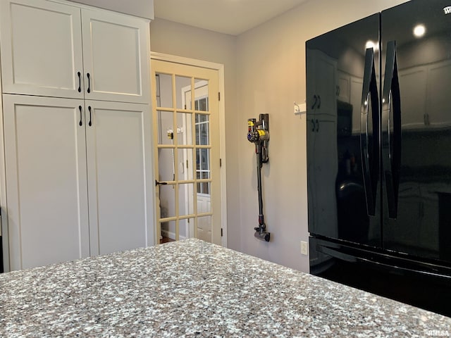 kitchen with white cabinets, stone countertops, and freestanding refrigerator