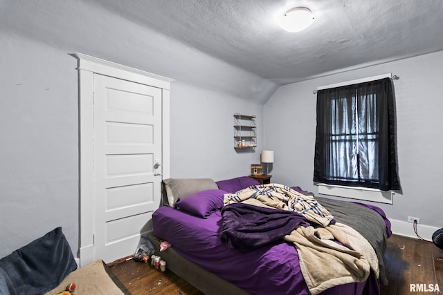 bedroom with vaulted ceiling, wood-type flooring, and a textured ceiling