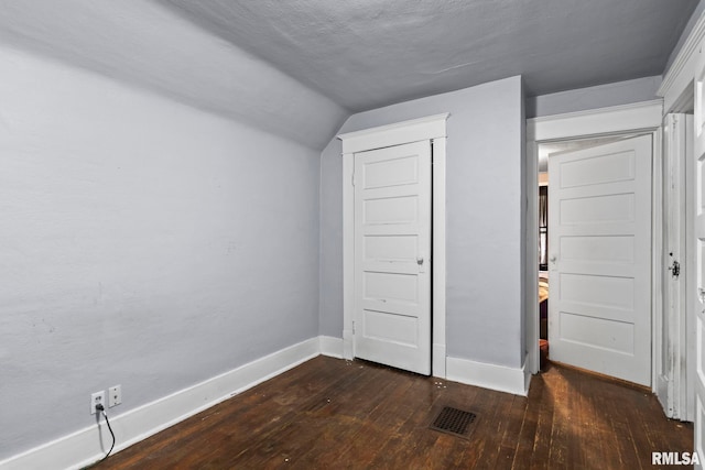 unfurnished bedroom with dark wood-style floors, visible vents, lofted ceiling, and baseboards