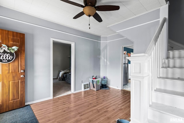 foyer with visible vents, a ceiling fan, wood finished floors, crown molding, and stairs