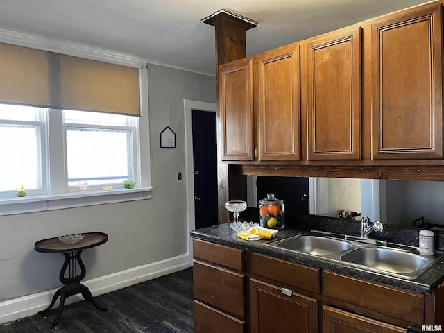 kitchen featuring a sink, dark countertops, dark wood finished floors, brown cabinetry, and baseboards