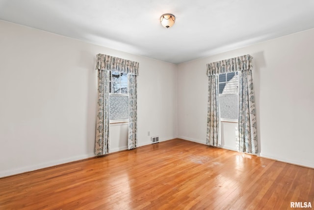 unfurnished room featuring visible vents, baseboards, a healthy amount of sunlight, and hardwood / wood-style floors