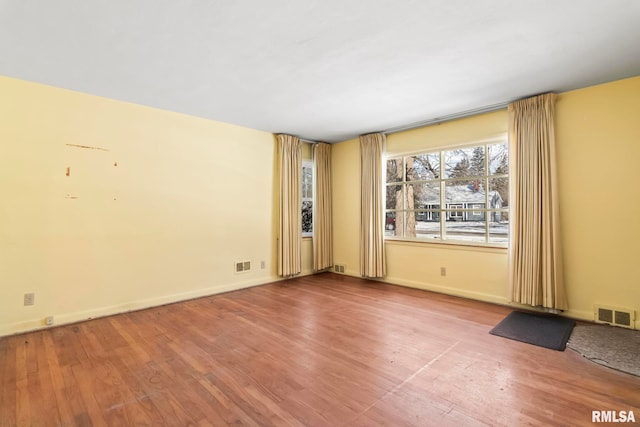 unfurnished room featuring wood finished floors, visible vents, and baseboards