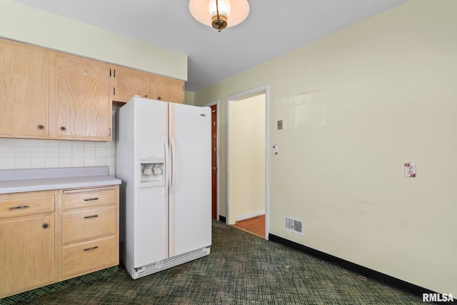 kitchen with visible vents, light brown cabinetry, light countertops, white fridge with ice dispenser, and backsplash