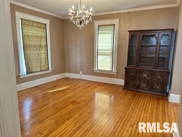 unfurnished room featuring hardwood / wood-style floors, an inviting chandelier, baseboards, and ornamental molding