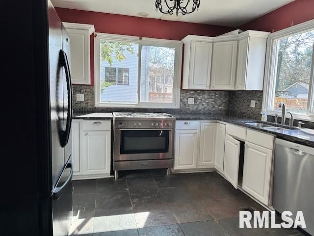 kitchen with a sink, stainless steel appliances, white cabinets, stone finish flooring, and tasteful backsplash