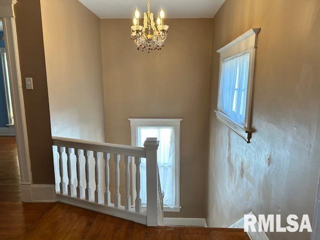 stairway with a wealth of natural light, an inviting chandelier, and wood finished floors