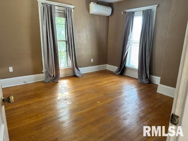 unfurnished room featuring baseboards, an AC wall unit, and wood finished floors