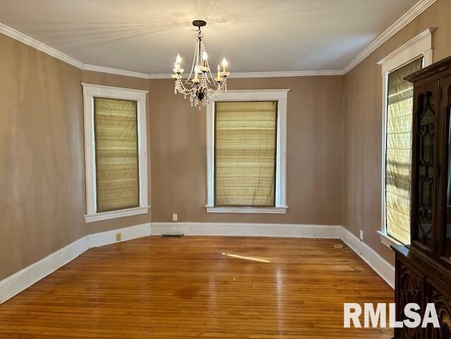 unfurnished dining area with a notable chandelier, wood finished floors, and crown molding