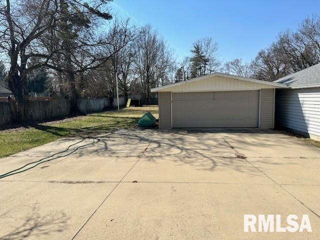 garage featuring concrete driveway and fence