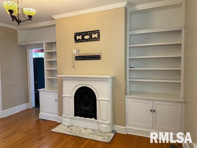 unfurnished living room with baseboards, an inviting chandelier, wood finished floors, and crown molding