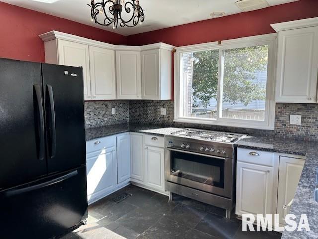 kitchen with a notable chandelier, high end stainless steel range, white cabinetry, freestanding refrigerator, and decorative backsplash