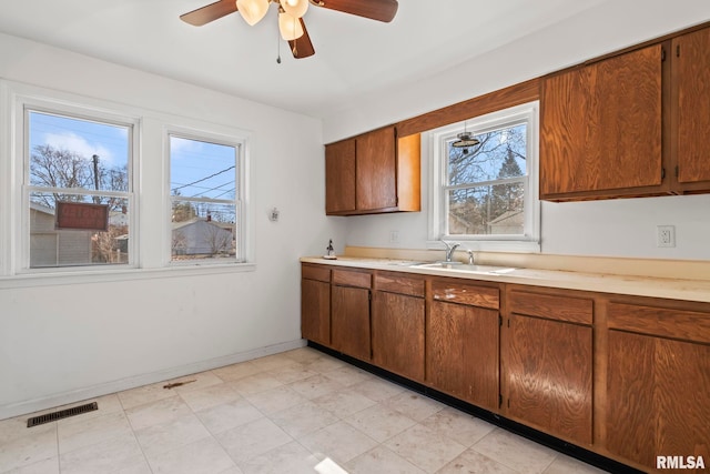 kitchen with visible vents, a sink, light countertops, baseboards, and ceiling fan