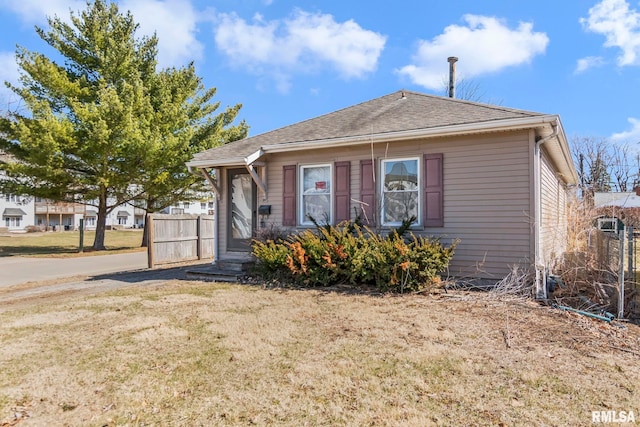 bungalow-style house with roof with shingles, a front yard, and fence