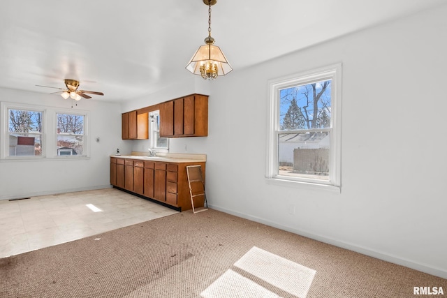 kitchen featuring a sink, light countertops, pendant lighting, light carpet, and brown cabinets