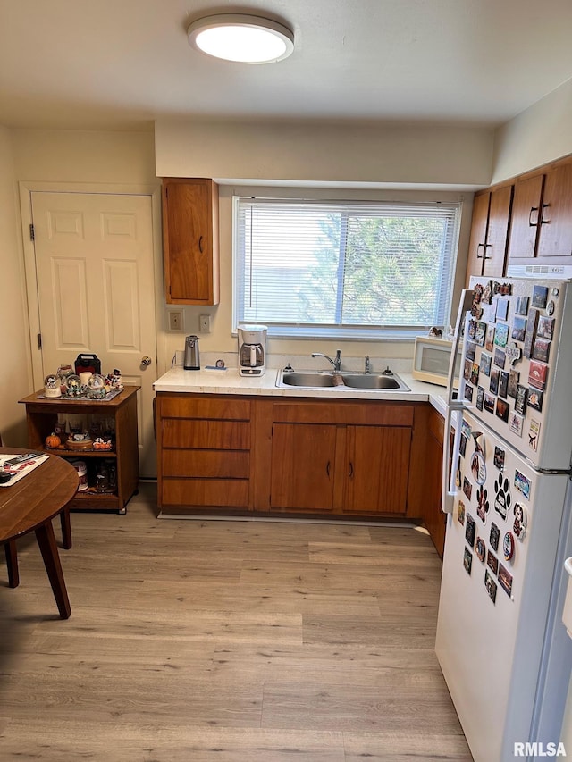 kitchen featuring white appliances, brown cabinetry, light wood finished floors, a sink, and light countertops