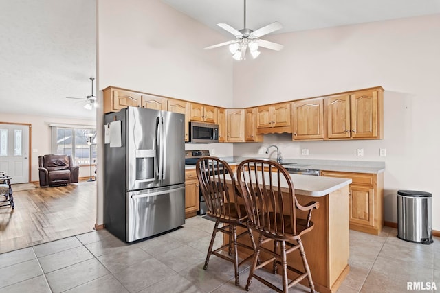 kitchen with a kitchen island, stainless steel appliances, light countertops, light tile patterned floors, and ceiling fan