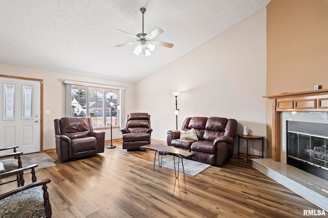 living room with ceiling fan, light wood-type flooring, a premium fireplace, a textured ceiling, and high vaulted ceiling