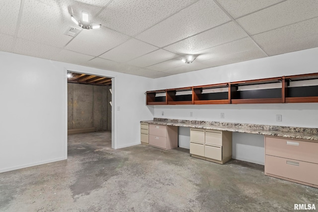 interior space with a drop ceiling, visible vents, unfinished concrete flooring, and built in desk