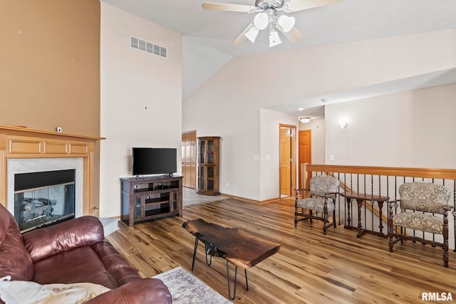 living area with wood finished floors, visible vents, high vaulted ceiling, ceiling fan, and a glass covered fireplace