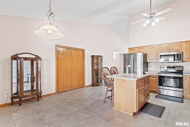 kitchen with a kitchen island, a kitchen bar, light countertops, stainless steel appliances, and a ceiling fan