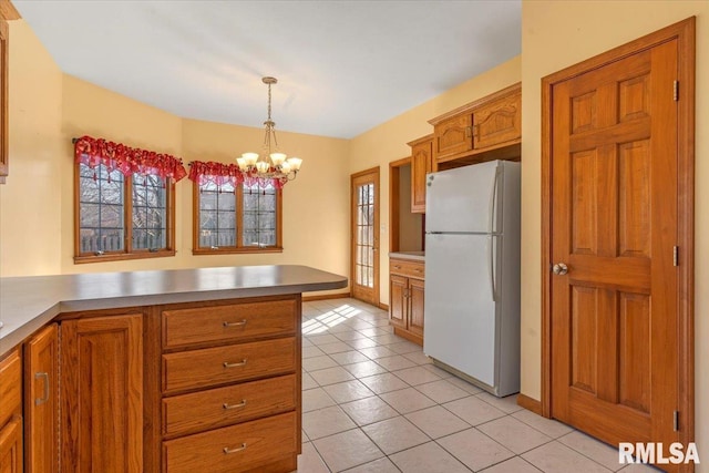 kitchen with a chandelier, pendant lighting, light countertops, brown cabinets, and freestanding refrigerator