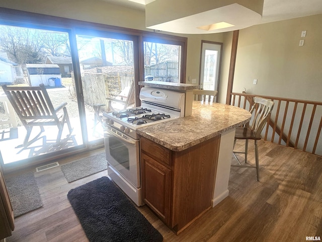 kitchen with wood finished floors, brown cabinetry, visible vents, white gas range oven, and a kitchen bar